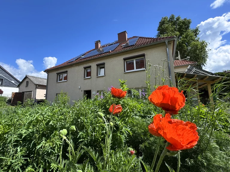 Die Naturheilpraxis befindet sich im Erdgeschoss des Hauses. Vor dem Haus blühen Wildblumen.