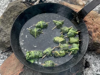 Wildkräuterküche auf offenem Feuer. Hier werden auf offenen Feuer Beinwellblätter mit Feta in Öl gebraten.