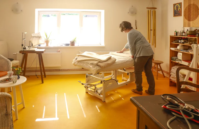 Die im gelblichen Ton gehaltene Praxis ist von Sonne durchflutet. Im Mittelpunkt des Raumes steht die Massageliege.